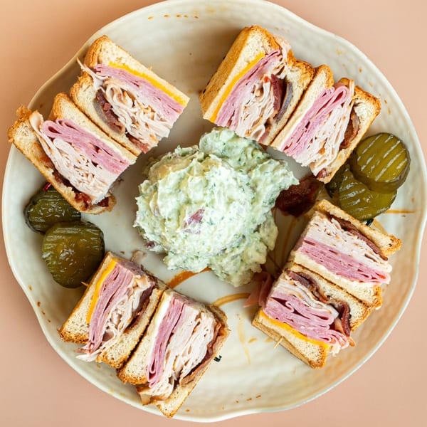 Club sandwiches with ham, turkey, cheese, and bacon, served with potato salad and pickles.