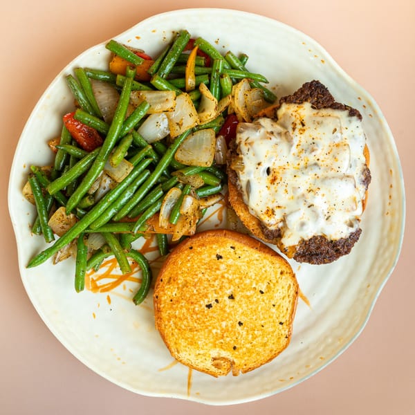 A deli burger with melted cheese and a side of green beans and onions on a white plate.