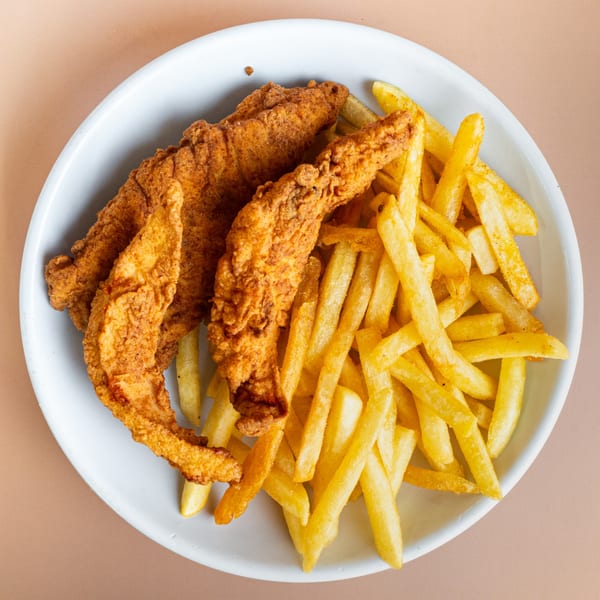 Crispy fried chicken tenders and golden french fries on a white plate from Pinegrove Market & Deli.