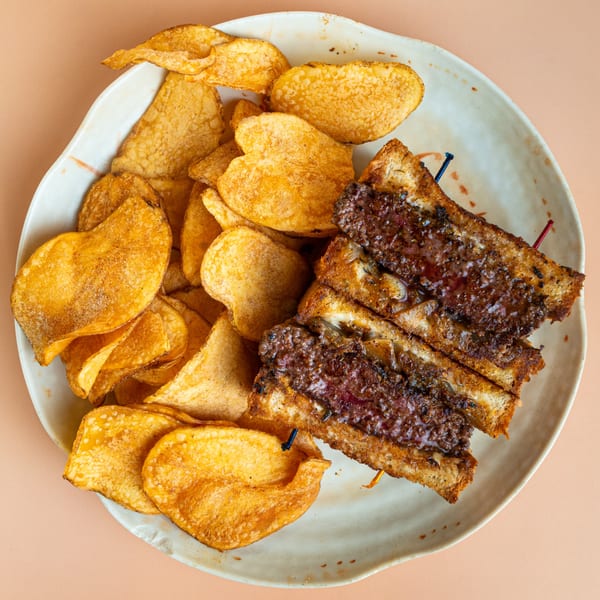 A grilled patty melt sandwich with melted cheese and onions, served with a side of potato chips.
