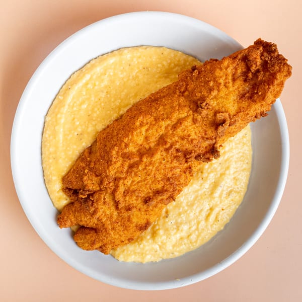 Crispy fried fish fillet served over a bed of creamy grits in a white bowl from Pinegrove Market & Deli.