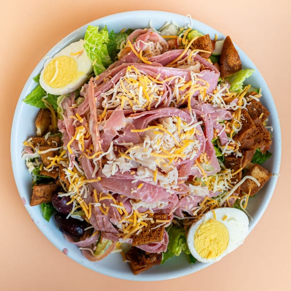 Overhead view of a deli salad with ham, cheese, croutons, and hard-boiled eggs.