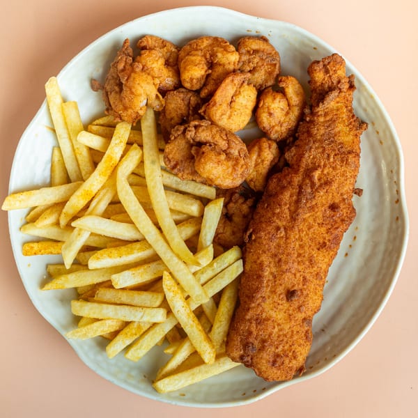 A plate of golden-brown fried fish, popcorn shrimp, and french fries from Pinegrove Market & Deli.
